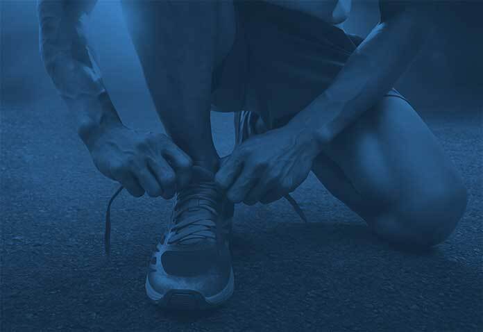 Duotone black and blue image of man timing up his shoelaces preparing to go for a run
