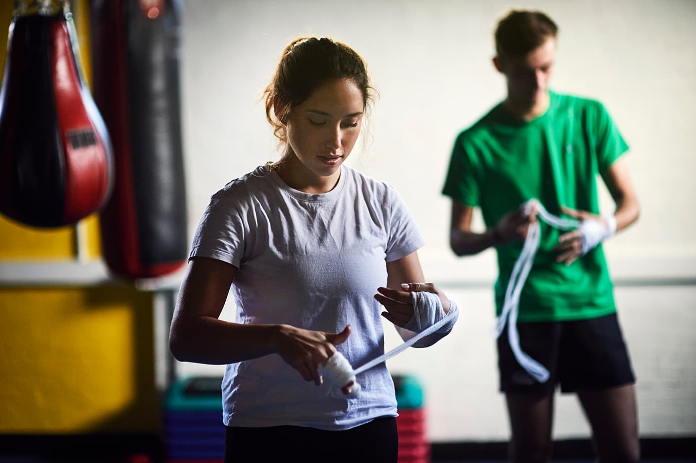 A women and man preparing their hands for boxing in a boxing gym with boxing bags in the background